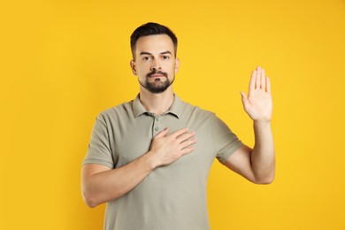 Photo of Man making promise with raised hand on orange background. Oath gesture