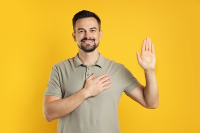 Photo of Man making promise with raised hand on orange background. Oath gesture