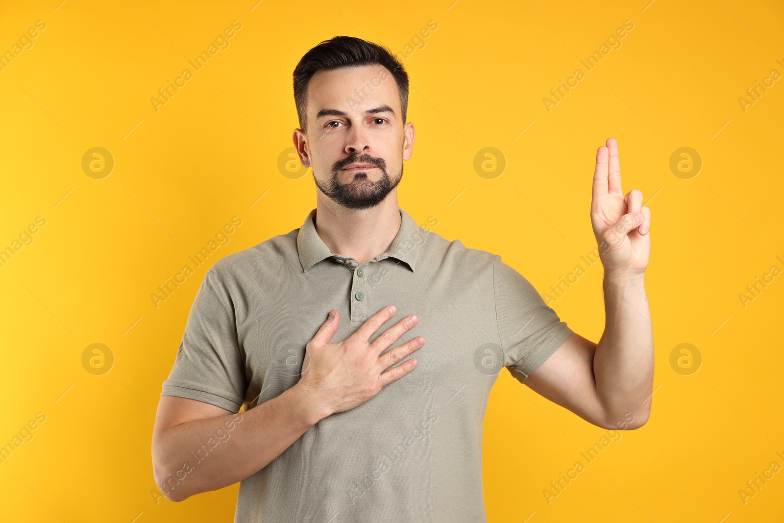 Photo of Man showing oath gesture on orange background. Making promise