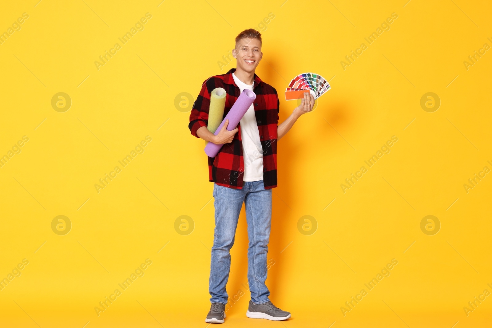 Photo of Young decorator with color palettes and rolls of wallpaper on orange background