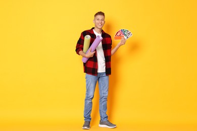 Photo of Young decorator with color palettes and rolls of wallpaper on orange background