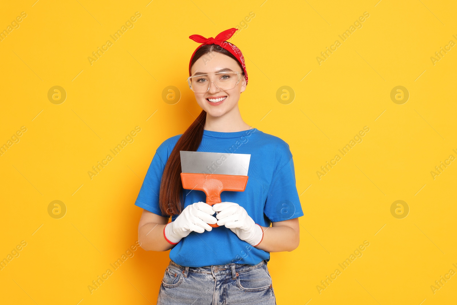 Photo of Portrait of young decorator with putty knife on orange background