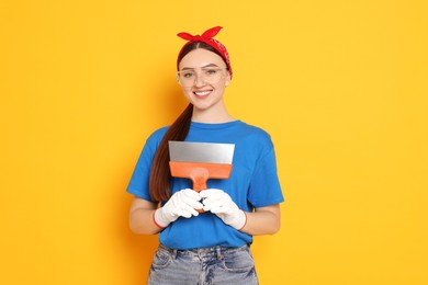 Photo of Portrait of young decorator with putty knife on orange background