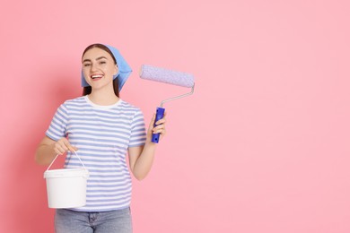 Photo of Portrait of young decorator with paint roller and bucket on pink background, space for text