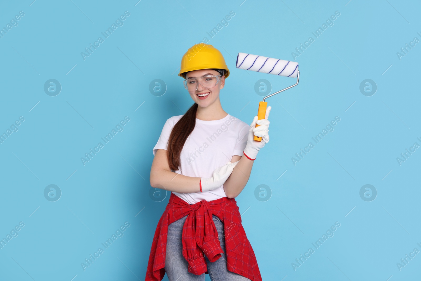 Photo of Portrait of young decorator with paint roller on light blue background