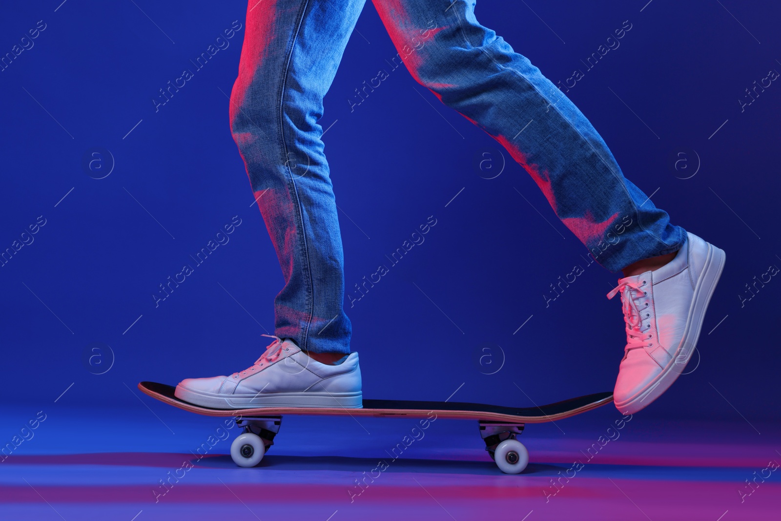 Photo of Man riding skateboard in color lights against blue background, closeup