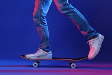 Photo of Man riding skateboard in color lights against blue background, closeup