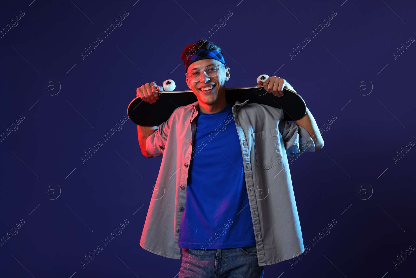 Photo of Happy man with skateboard in color lights against blue background