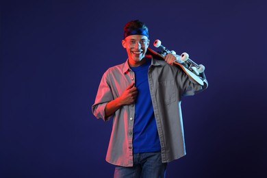 Photo of Happy man with skateboard in color lights against blue background