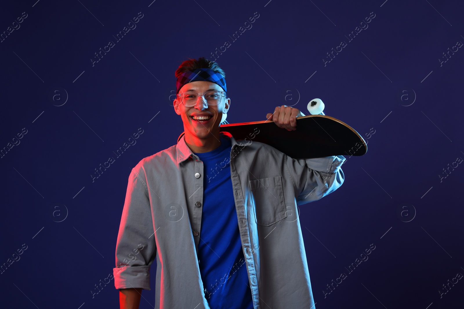 Photo of Happy man with skateboard in color lights against blue background