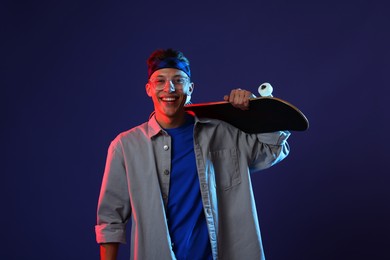 Photo of Happy man with skateboard in color lights against blue background