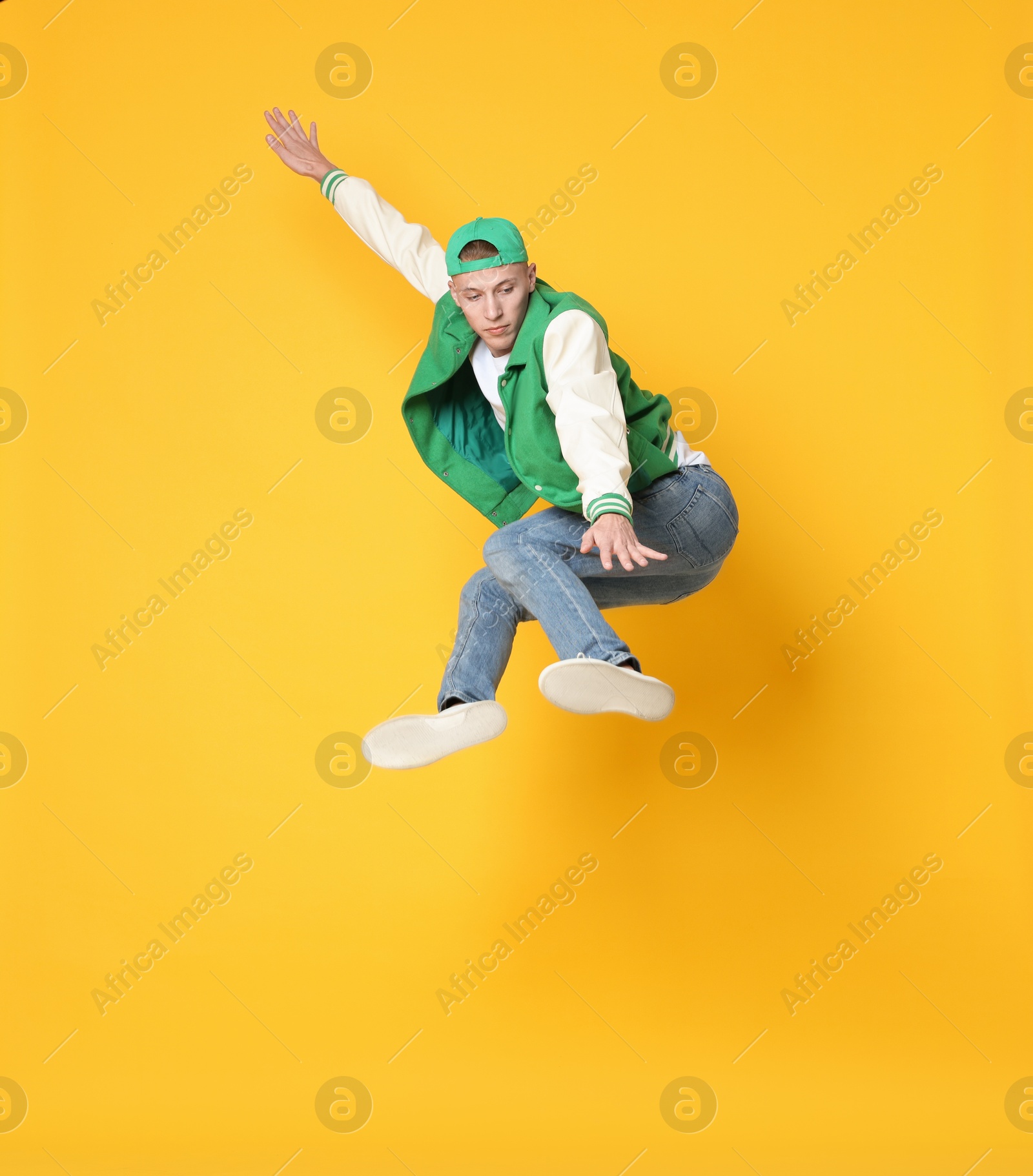 Photo of Handsome young skater jumping on orange background