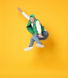 Photo of Handsome young skater jumping on orange background