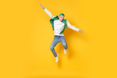 Photo of Handsome young skater jumping on orange background