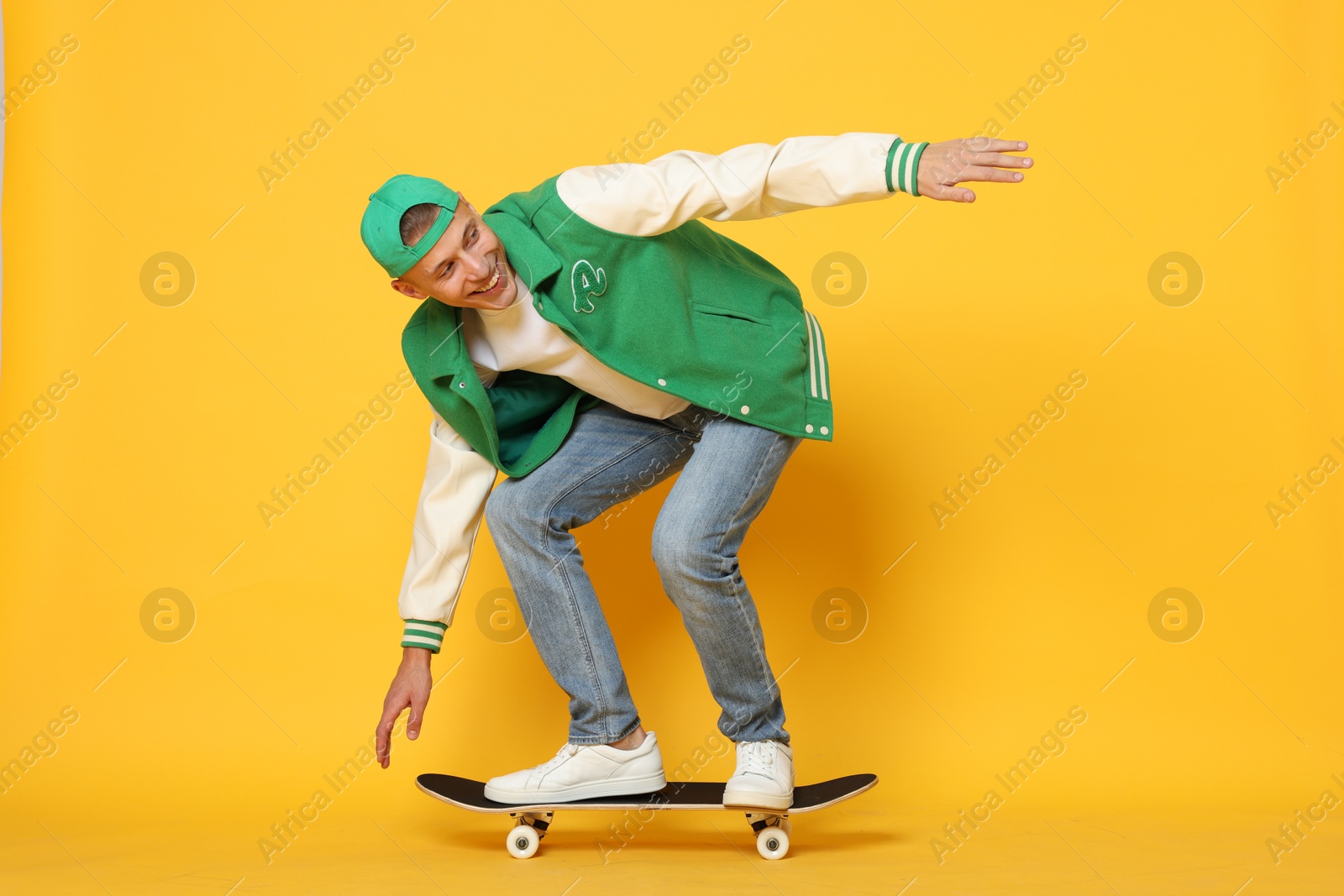 Photo of Happy man riding skateboard on orange background