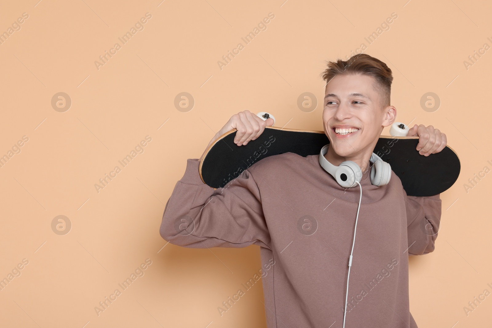 Photo of Happy man with skateboard and headphones on beige background. Space for text