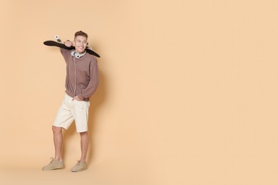 Photo of Happy man with skateboard and headphones on beige background. Space for text