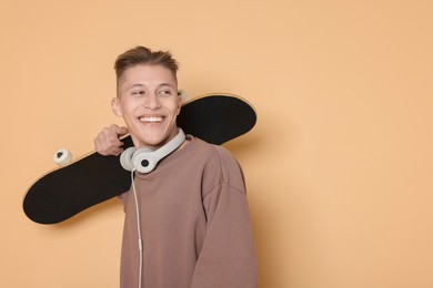 Photo of Happy man with skateboard and headphones on beige background. Space for text