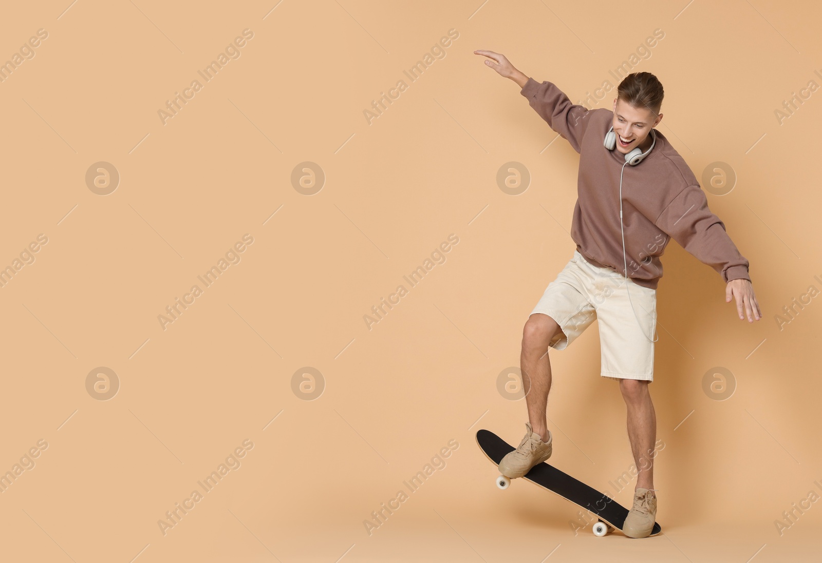 Photo of Happy man riding skateboard on beige background. Space for text