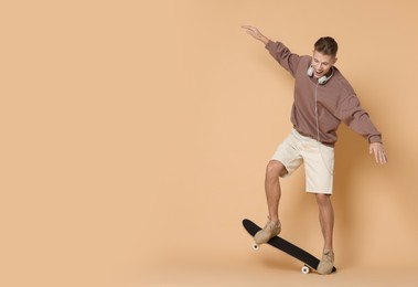 Photo of Happy man riding skateboard on beige background. Space for text