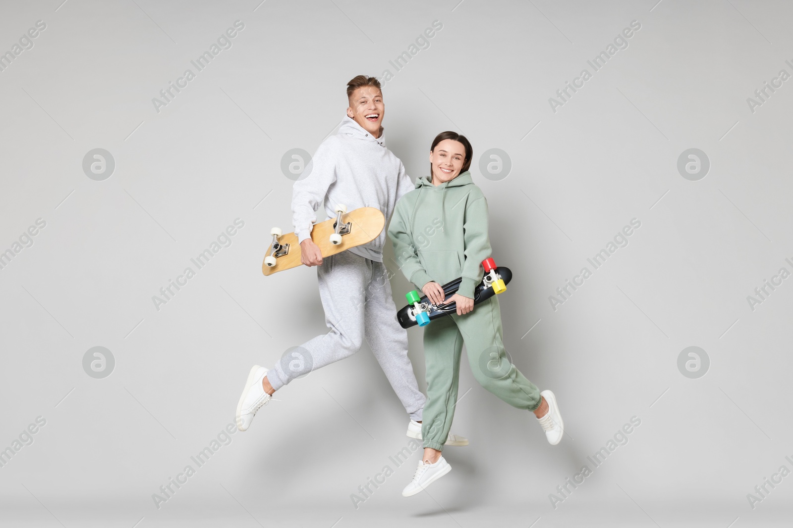 Photo of Happy friends jumping with skateboards on light grey background