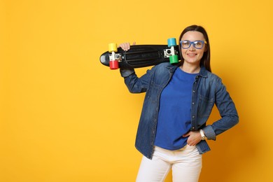 Photo of Smiling woman with penny board on orange background. Space for text