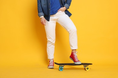 Photo of Woman with penny board on orange background, closeup