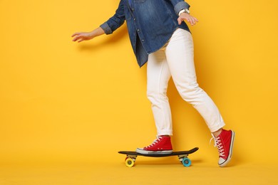 Photo of Woman riding penny board on orange background, closeup. Space for text