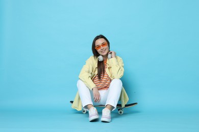 Photo of Smiling woman sitting on skateboard against light blue background