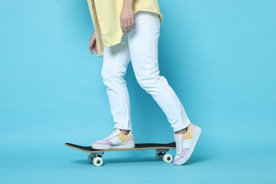 Photo of Woman riding skateboard on light blue background, closeup