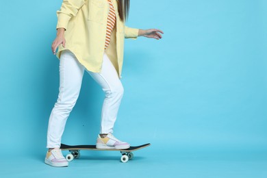 Photo of Woman riding skateboard on light blue background, closeup. Space for text