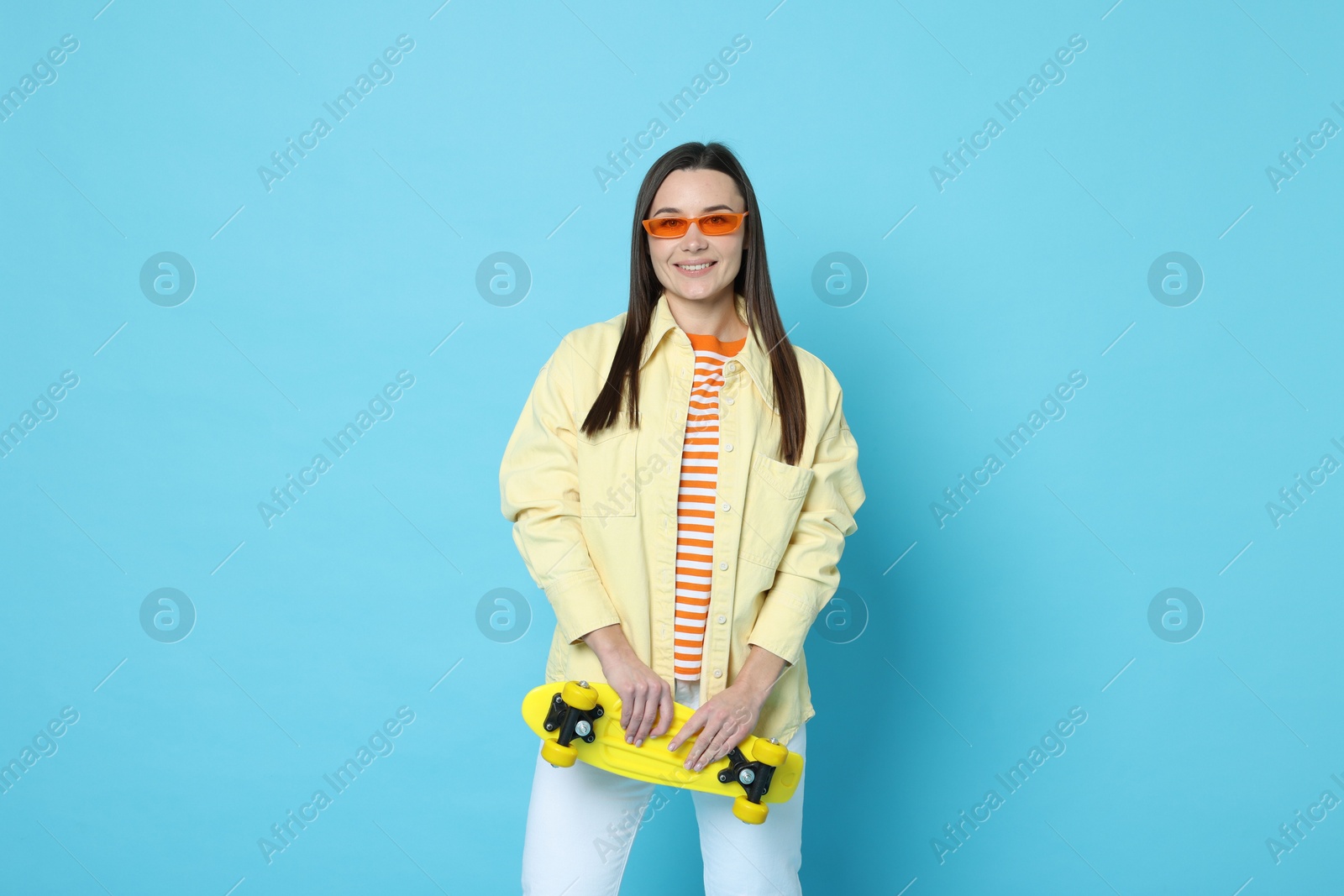 Photo of Smiling woman with penny board on light blue background