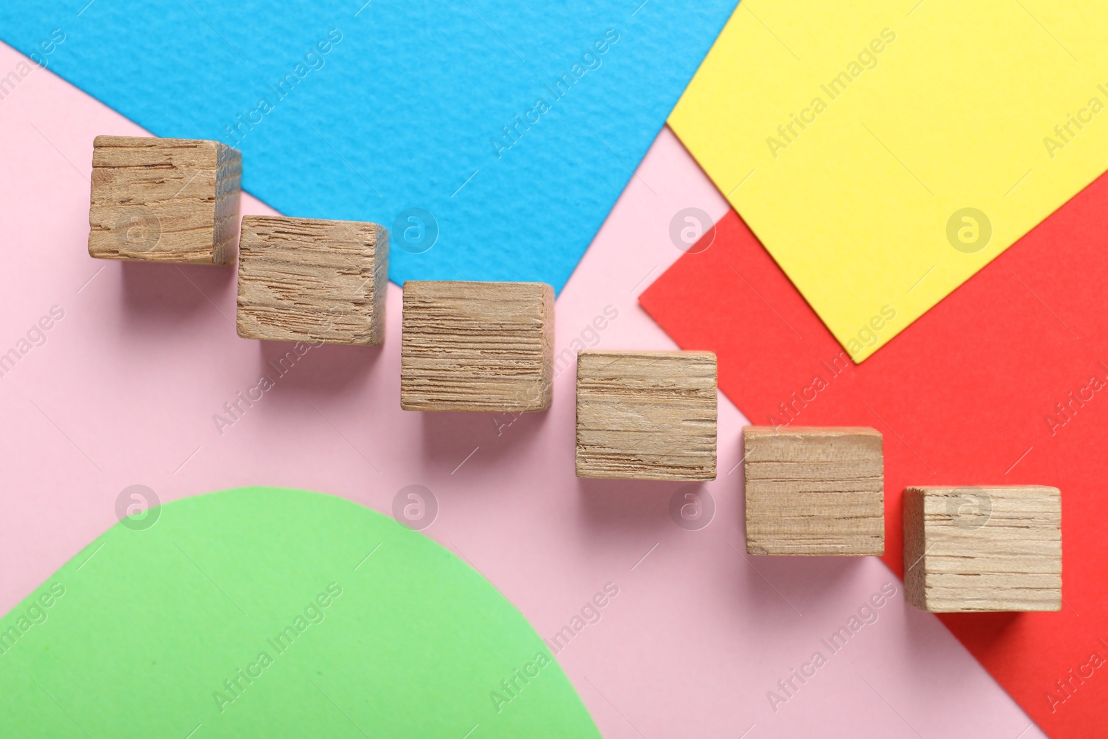 Photo of Wooden cubes and colorful sheets of paper on pink background, flat lay