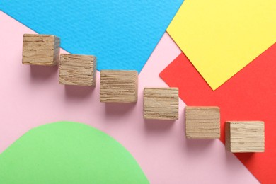 Photo of Wooden cubes and colorful sheets of paper on pink background, flat lay