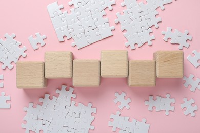 Photo of Wooden cubes and puzzle pieces on pink background, flat lay