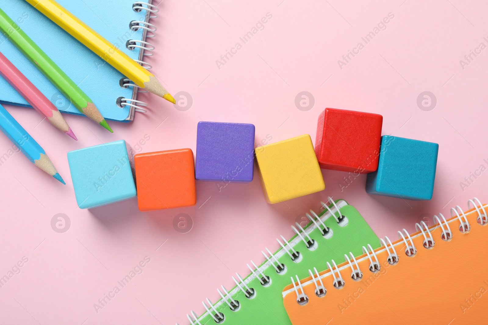 Photo of Colorful cubes, pencils and notebooks on pink background, flat lay