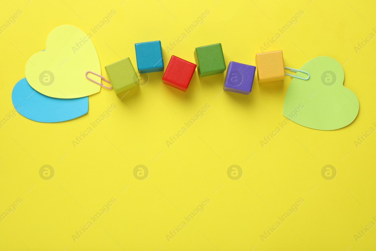 Photo of Colorful cubes and paper hearts on yellow background, flat lay. Space for text