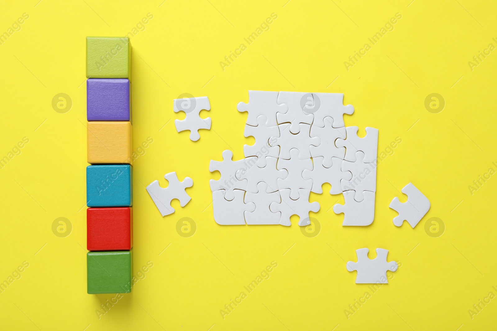 Photo of Colorful cubes and puzzle pieces on yellow background, flat lay