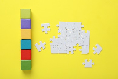 Photo of Colorful cubes and puzzle pieces on yellow background, flat lay