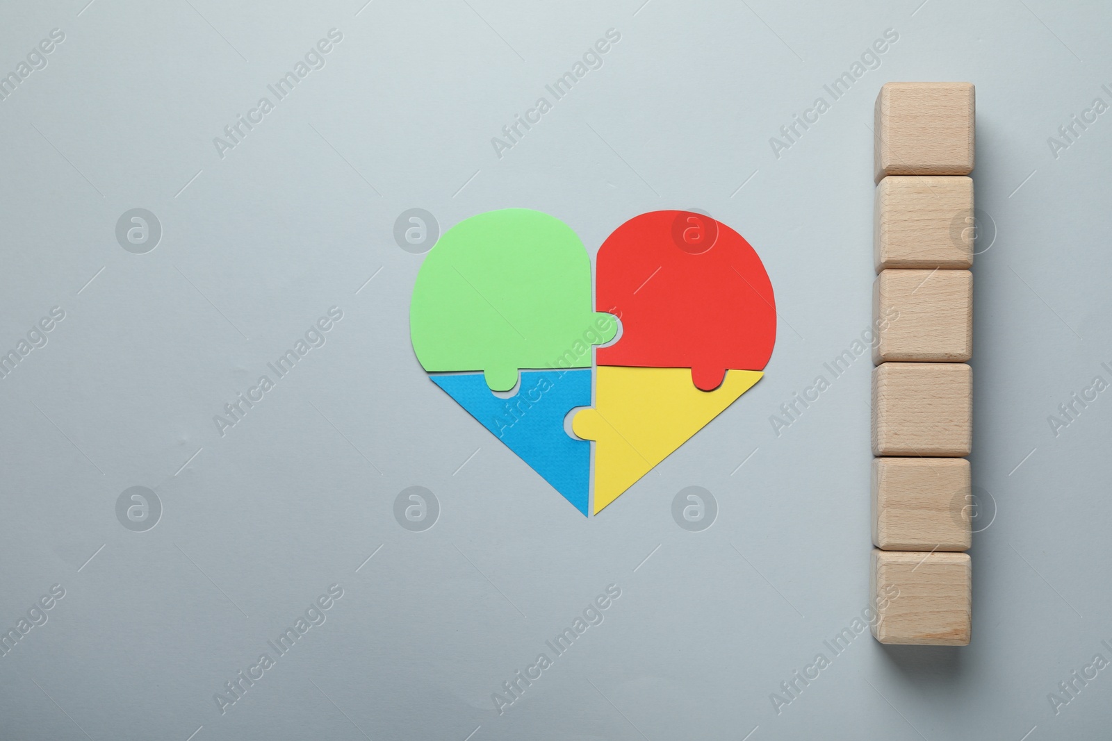 Photo of Wooden cubes and heart made of puzzle pieces on grey background, flat lay. Space for text