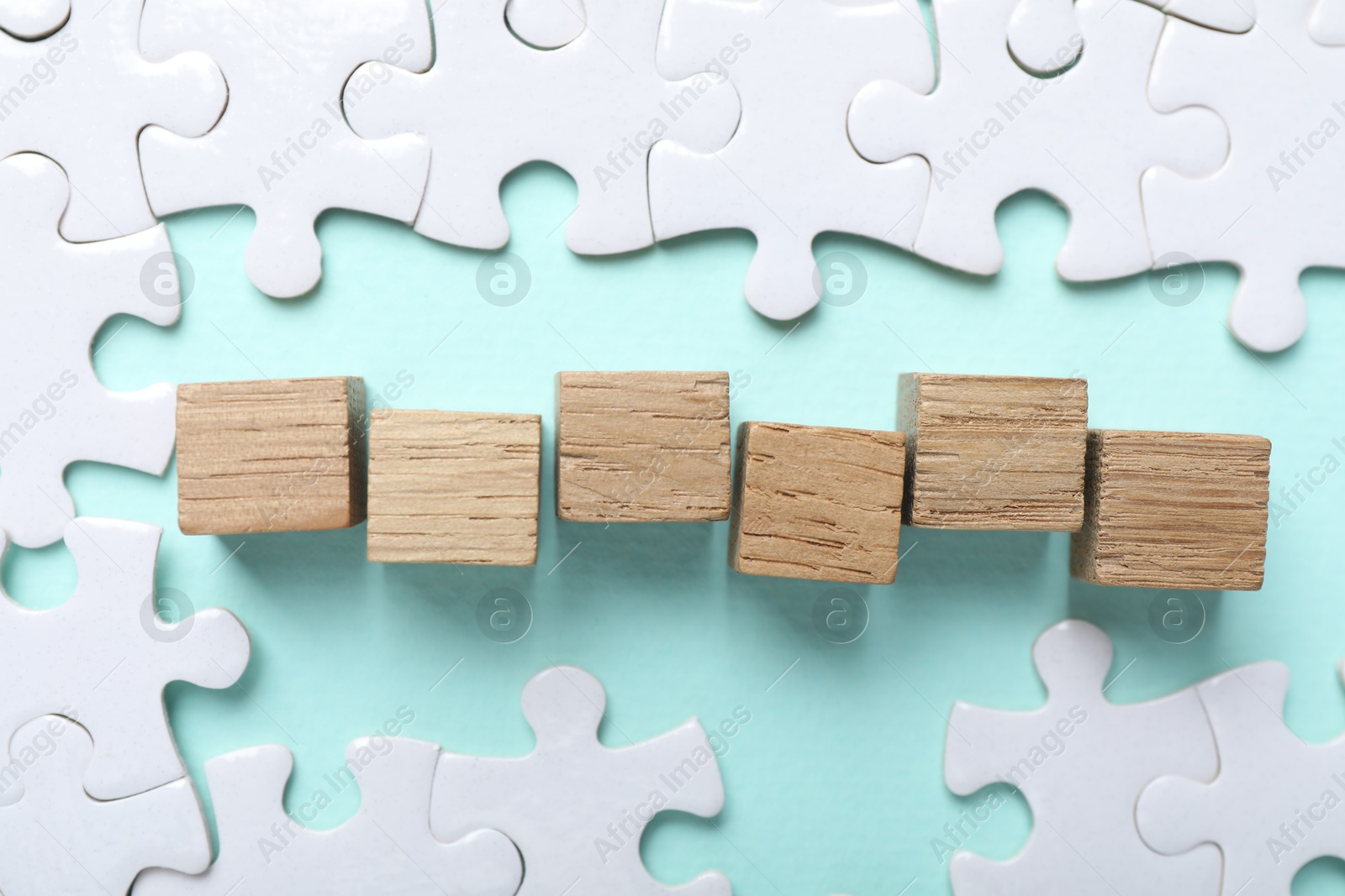 Photo of Wooden cubes and puzzle pieces on light blue background, flat lay