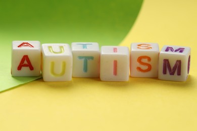 Photo of Word Autism made with colorful cubes and green sheet of paper on yellow background, closeup