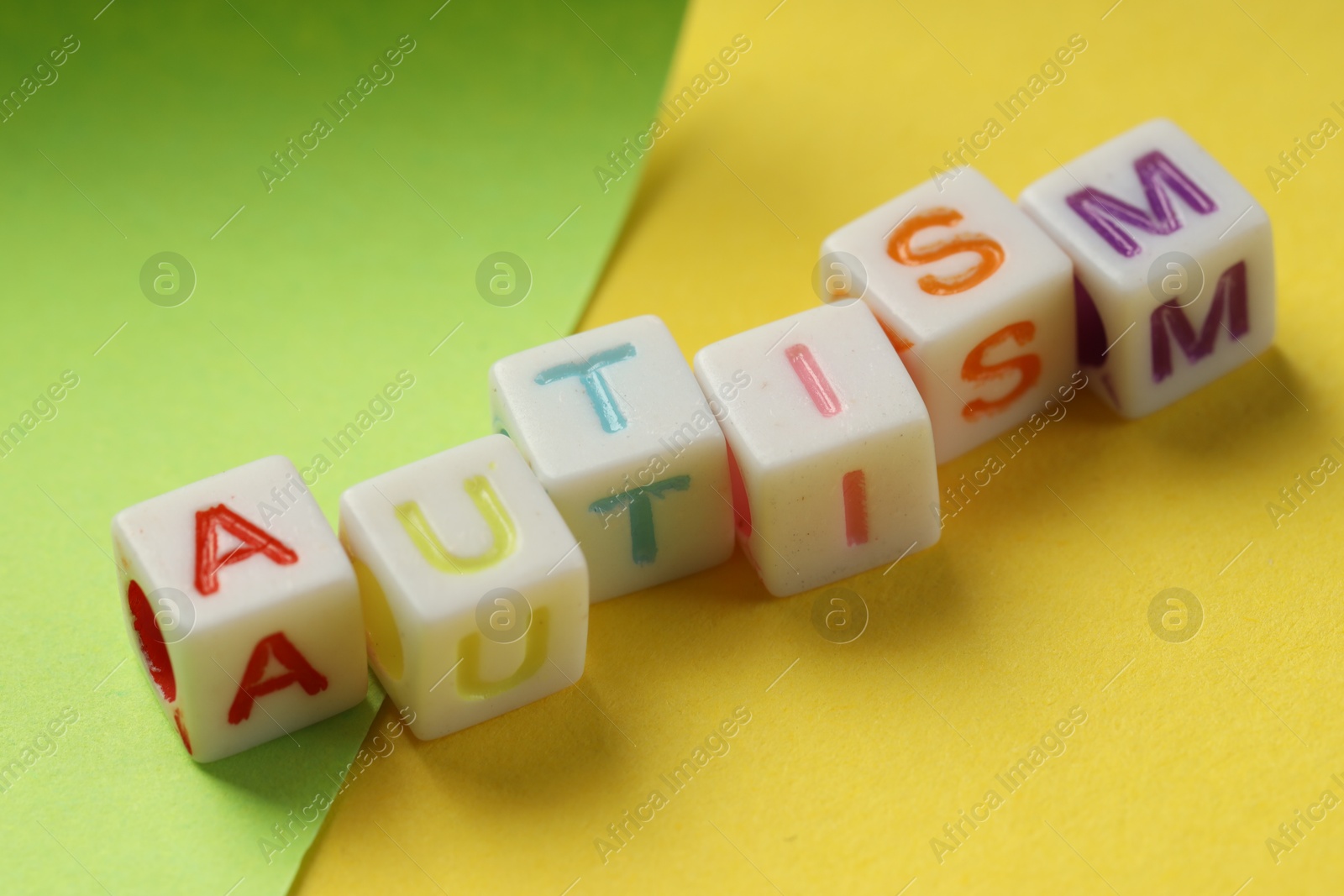 Photo of Word Autism made with colorful cubes and green sheet of paper on yellow background, closeup