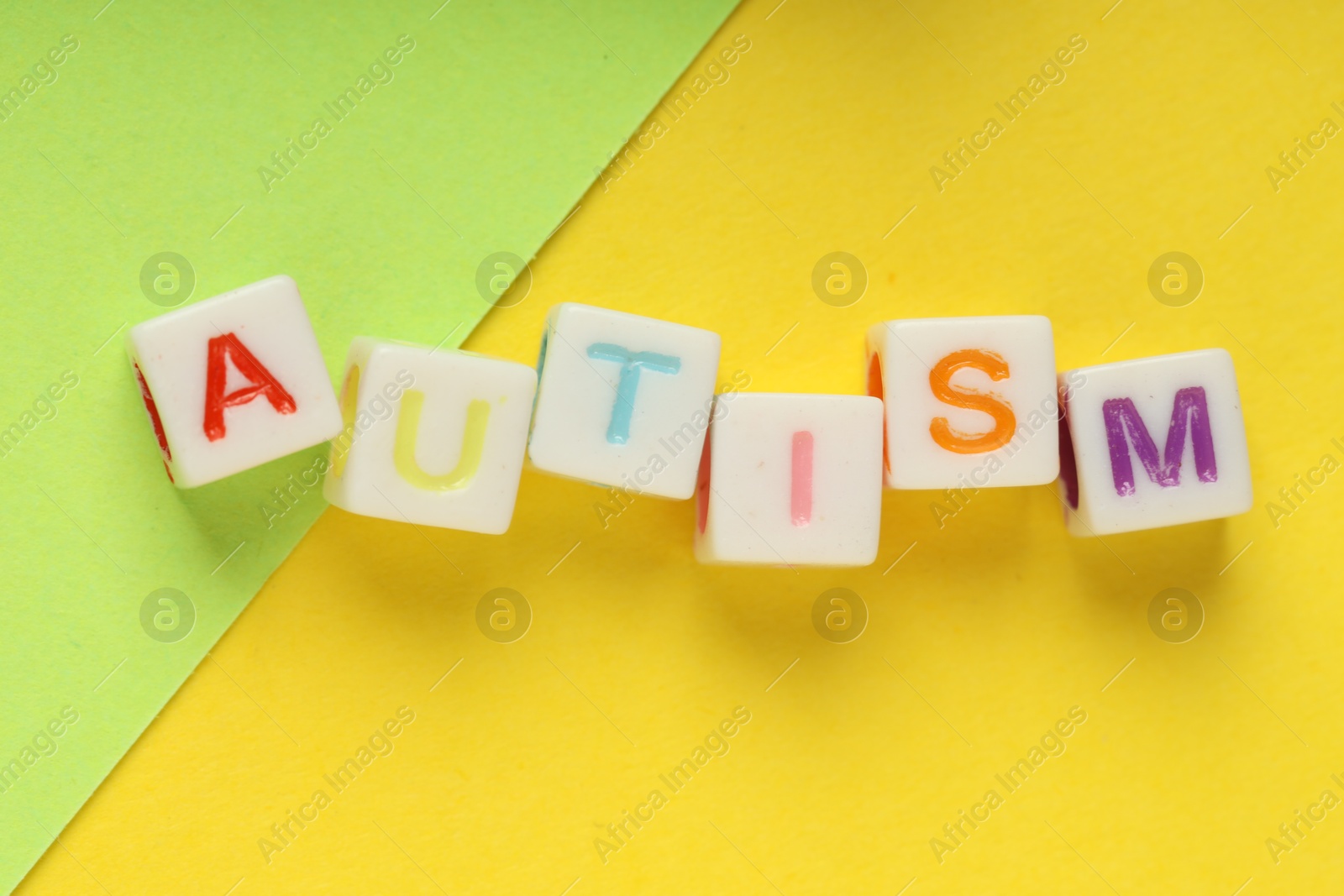 Photo of Word Autism made with colorful cubes and green sheet of paper on yellow background, top view