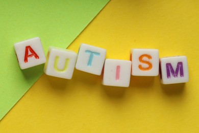 Photo of Word Autism made with colorful cubes and green sheet of paper on yellow background, top view