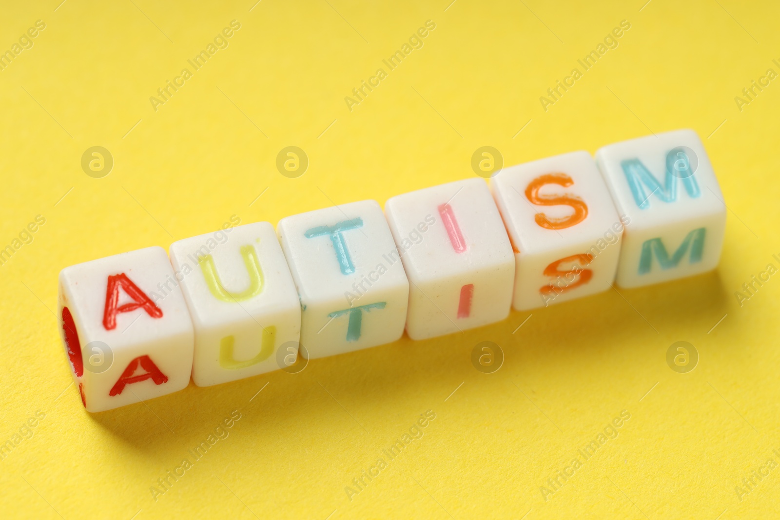 Photo of Word Autism made with colorful cubes on yellow background, closeup