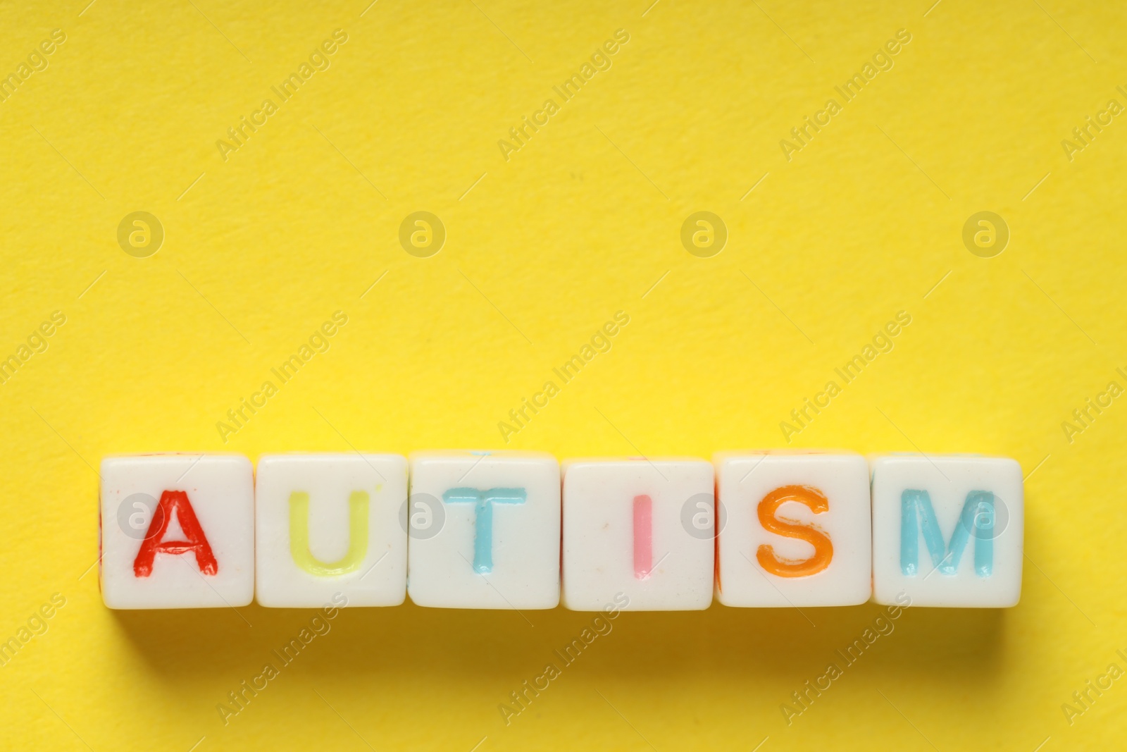 Photo of Word Autism made with colorful cubes on yellow background, flat lay. Space for text