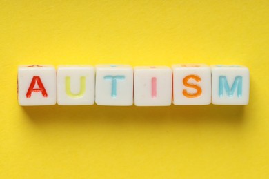 Photo of Word Autism made with colorful cubes on yellow background, top view