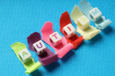 Photo of Word Autism made with cubes and cut colorful paper on light blue background, closeup