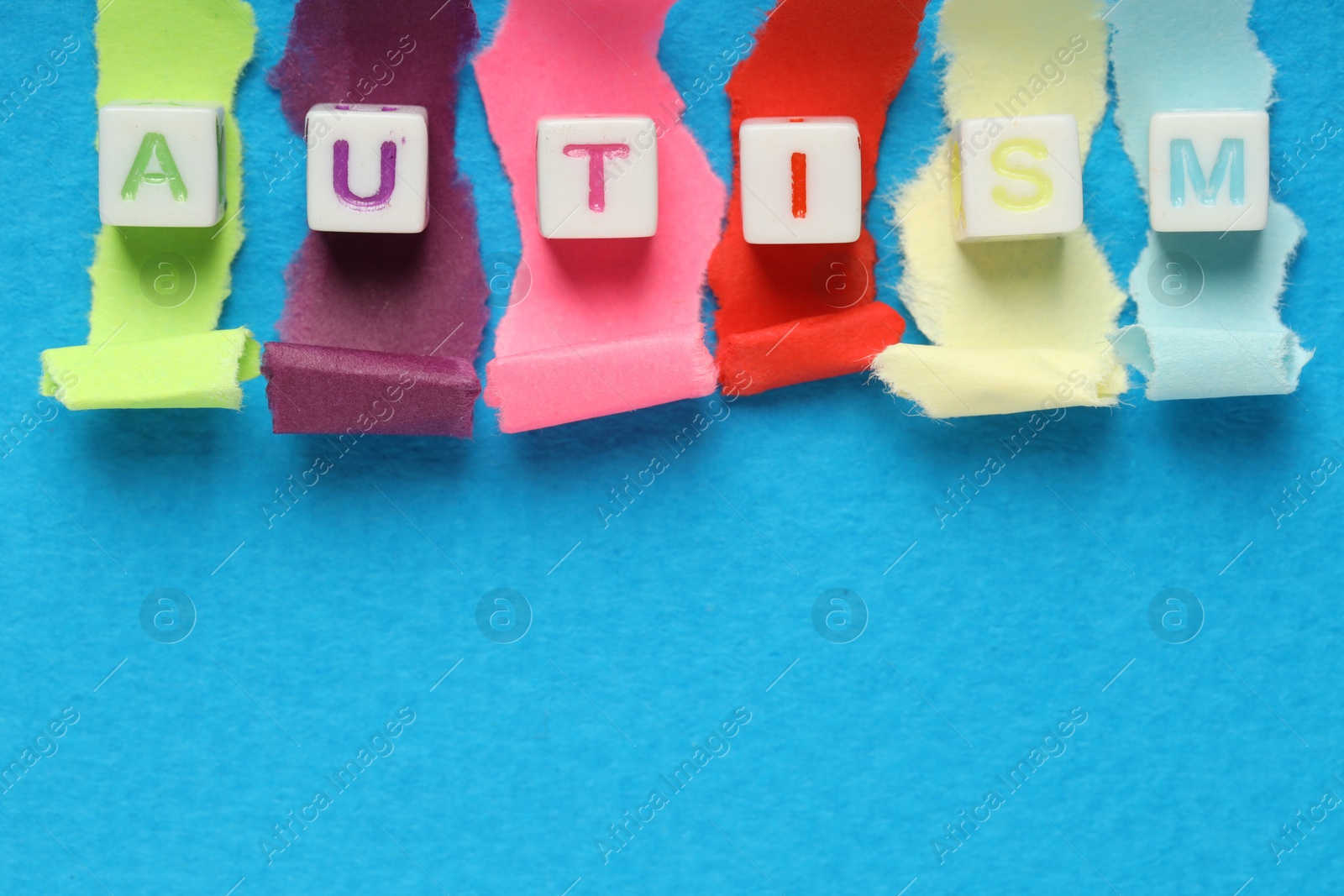 Photo of Word Autism made with cubes and cut colorful paper on light blue background, flat lay. Space for text